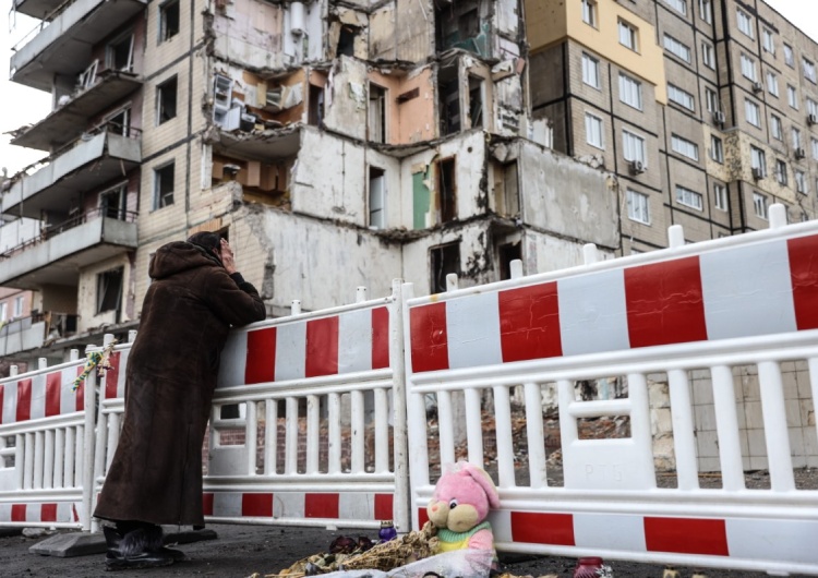 Kobieta stoi przed zniszczonym blokiem w Dnieprze. Mija rok od rosyjskiej inwazji na Ukrainę. Ludobójstwa, tysiące ofiar, miliony uchodźców